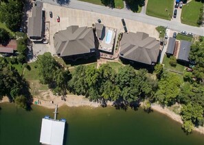 Vista aérea de uma área residencial com duas casas grandes, uma piscina e um píer que se estende sobre a água.