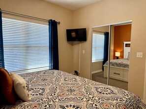 Quarto com cama, televisão presa na parede e espelho refletindo o ambiente.