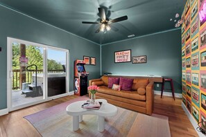 Un salon avec un ventilateur de plafond, un canapé marron, une table basse ornée d’un vase de fleurs et un mur décoré de cassettes audio colorées.