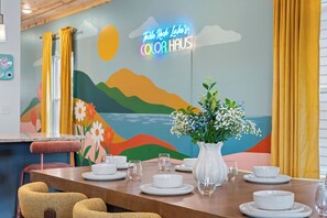 Un coin repas avec une table dressée pour quatre personnes, un vase rempli de fleurs et une fresque colorée sur le mur.
