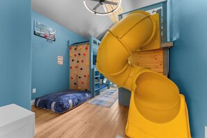 Una habitación con literas, una pared de escalar y un tobogán amarillo.