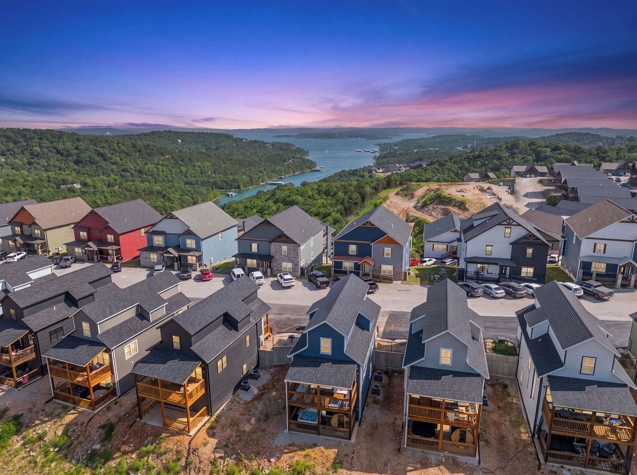 A residential area with multiple houses, a parking lot, and a view of a lake and forested hills.