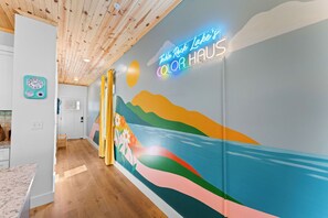 Un couloir orné d’une fresque colorée, d’une enseigne au néon et doté d’un plafond en bois.