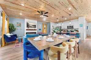 Una cocina moderna con armarios blancos, una isla central y una zona de comedor con sillas azules y una mesa de madera.
