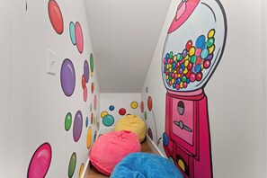 Una stanza giochi per bambini con decorazioni murali colorate, un sacco di biglie e una macchina per le caramelle.