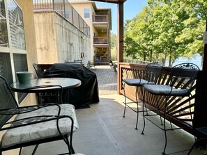 An outdoor patio with tables and chairs, a grill, and a view of a building and trees. - Lakefront 3BR condo at Table Rock Lake with pool, patio, and resort perks. (Hollister)