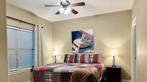 A bedroom with a bed, two bedside lamps, a ceiling fan, a window with blinds, and a painting on the wall. - Lakefront 3BR condo at Table Rock Lake with pool, patio, and resort perks. (Hollister)
