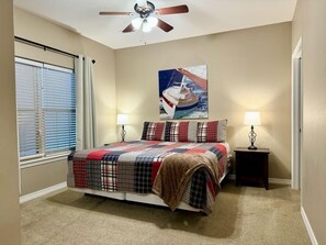 Ein Schlafzimmer mit einem Bett, zwei Nachttischlampen, einem Deckenventilator, einem Fenster mit Jalousien und einem Bild an der Wand.