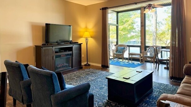 A living room with a flat-screen TV, dark-colored chairs, a coffee table, and a ceiling fan. - Lakefront 3BR condo at Table Rock Lake with pool, patio, and resort perks. (Hollister)
