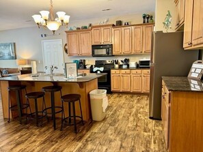 A kitchen with wooden cabinets, a central island with stools, a refrigerator, and a microwave. - Lakefront 3BR condo at Table Rock Lake with pool, patio, and resort perks. (Hollister)