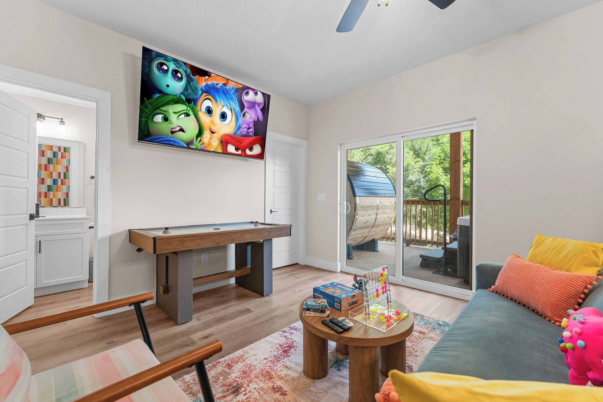 Een moderne woonkamer met een pooltafel, een televisie waarop geanimeerde personages te zien zijn, en uitzicht op een houten terras.