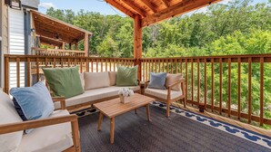 A covered outdoor seating area with a wooden deck, a sofa set, and a coffee table. - NEW Disney Lodge 4 min SDC+Hot tub • Sauna • Slide (Branson)