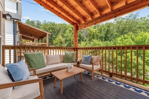 A covered outdoor seating area with a wooden deck, a sofa set, and a coffee table. - NEW Disney Lodge 4 min SDC+Hot tub • Sauna • Slide (Branson)