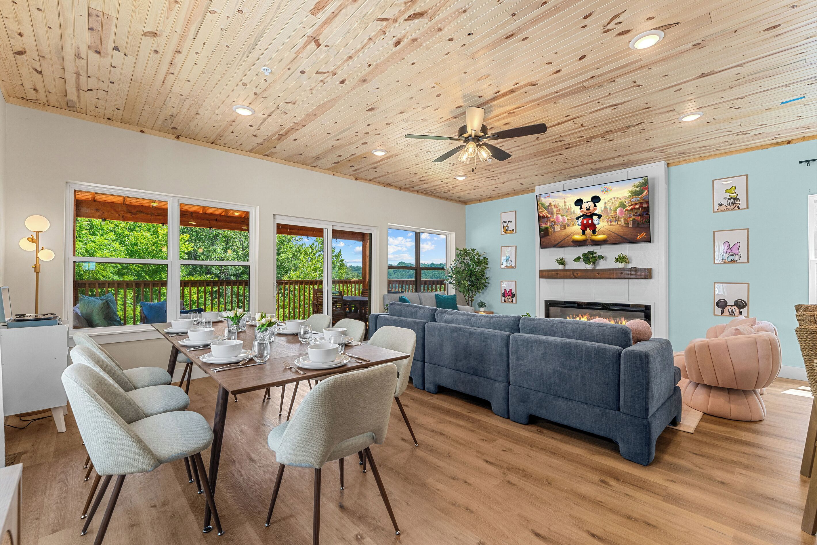 A spacious living area with a dining table set for four, a large grey sofa, and a flat-screen TV mounted on the wall.