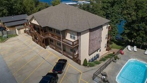 A multi-story building with a swimming pool, a parking lot, and a view of a lake. - Lakefront 3BR condo with pool, balcony, WiFi, and resort access. (Hollister)
