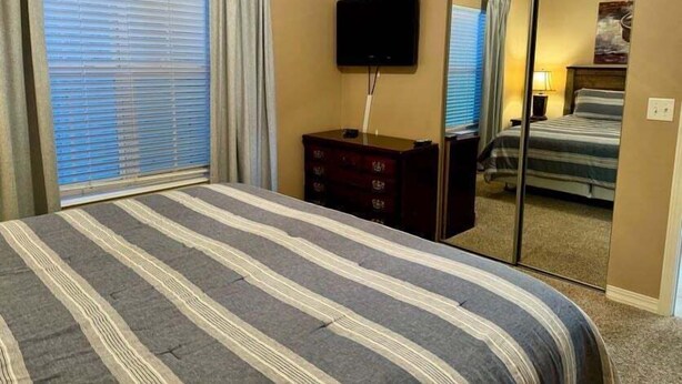 A hotel room with a bed, a dresser, a television, and a sliding door leading to a bathroom. - Lakefront 3BR condo with pool, balcony, WiFi, and resort access. (Hollister)
