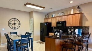 A kitchen with a central island, dining table, chairs, and a clock on the wall. - Lakefront 3BR condo with pool, balcony, WiFi, and resort access. (Hollister)