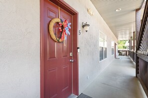 A red door with a wreath, a number '5' on the wall, and a covered porch with a railing. - 3BR lakefront condo with balcony, pool, and resort access (Hollister)