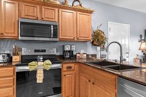A kitchen with wooden cabinets, a microwave, a stove, a sink, and a coffee maker. - 3BR lakefront condo with balcony, pool, and resort access (Hollister)
