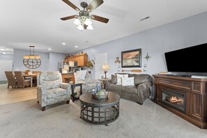 A living room with a fireplace, a television, and a dining area with wicker chairs. - 3BR lakefront condo with balcony, pool, and resort access (Hollister)