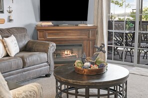A living room with a leather sofa, a flat-screen TV, a fireplace, and a round coffee table with decorative items. - 3BR lakefront condo with balcony, pool, and resort access (Hollister)