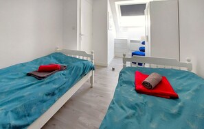 Quarto com duas camas, um guarda-roupa e uma secretária com cadeira.