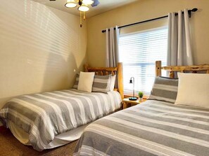 A room with two single beds, a nightstand, a lamp, and a window with curtains. - Lakefront 3BR condo with pool, balcony, fireplace, and resort views. (Hollister)