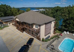 A multi-story building with a swimming pool, a parking lot, and a view of a lake. - Lakefront 3BR condo with pool, balcony, fireplace, and resort views. (Hollister)