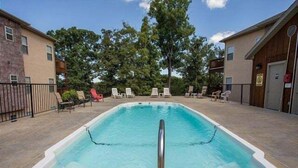 En rektangulär swimmingpool med ett metallräcke som fungerar som säkerhetsanordning, omgiven av solstolar och en stenlagd uteplats.