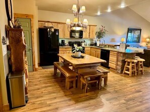 A kitchen with wooden cabinets, a black refrigerator, a wooden dining table with benches, and a built-in island with stools. - Lakefront 3BR condo with pool, balcony, fireplace, and resort views. (Hollister)