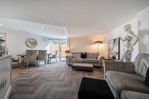 Un'ampia zona giorno con pavimento a spina di pesce, un divano, un tavolo da pranzo con sedie e uno specchio decorativo.