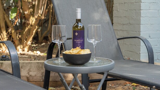 Een tafel met een schaal chips, twee glazen en een fles wijn.