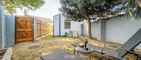 Een privé buitenruimte met een houten poort, een kleine tafel met een fles en glazen, en twee comfortabele stoelen.