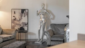 Een moderne woonkamer met een metalen sculptuur, een grijze bank en een eigentijds abstract schilderij.