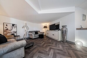 A modern living room with a herringbone floor, a sofa, a decorative statue, a flat-screen TV, and a large vase. - Annexe Bungalow, Sleeps 2 Maximum - Parking,Garden (Great Yarmouth)