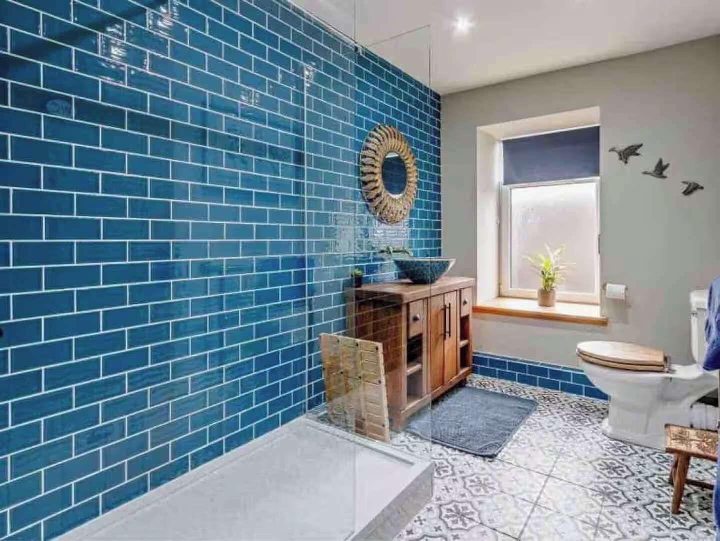 A bathroom with blue tiled walls, a wooden cabinet, a white toilet, and a patterned floor.