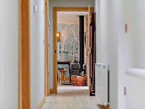 A hallway leading to a room with a fireplace, a window with a view of trees, and a wicker chair. - Cottage Sleeps 6 with Hot Tub and Bbq Hut (Lanark)