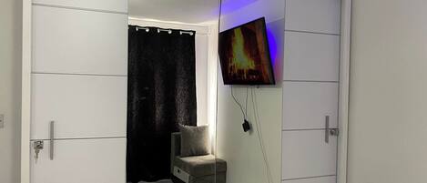 A room with a sliding closet door, a television mounted on the wall, and a small seating area with a cushion.