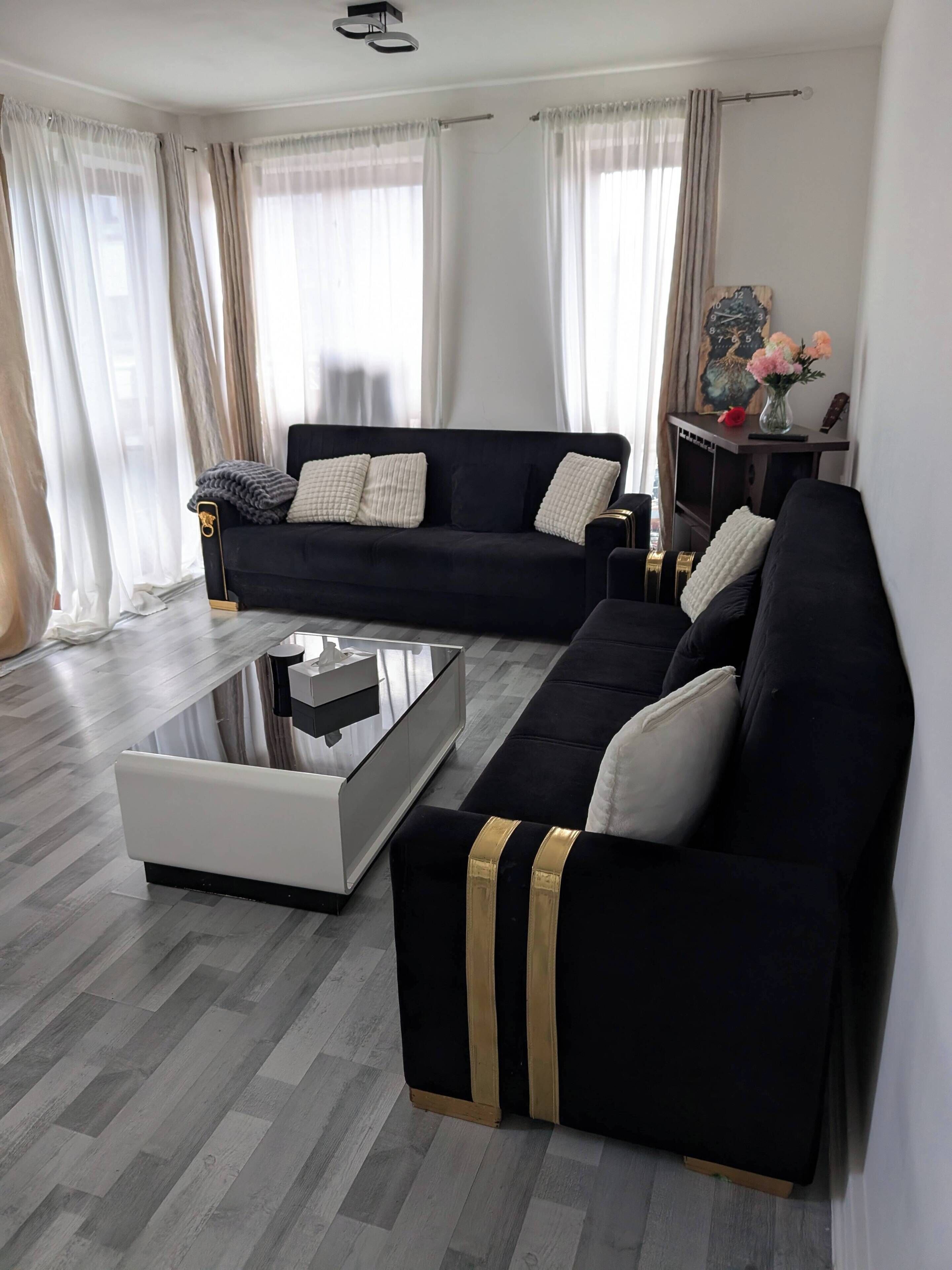 A modern living room with a black sofa, a white coffee table, and a wooden floor.