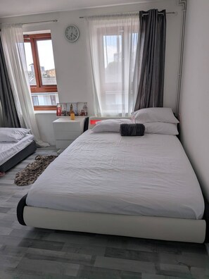 Una camera da letto con un letto, un comodino, una sveglia e una finestra con tende.