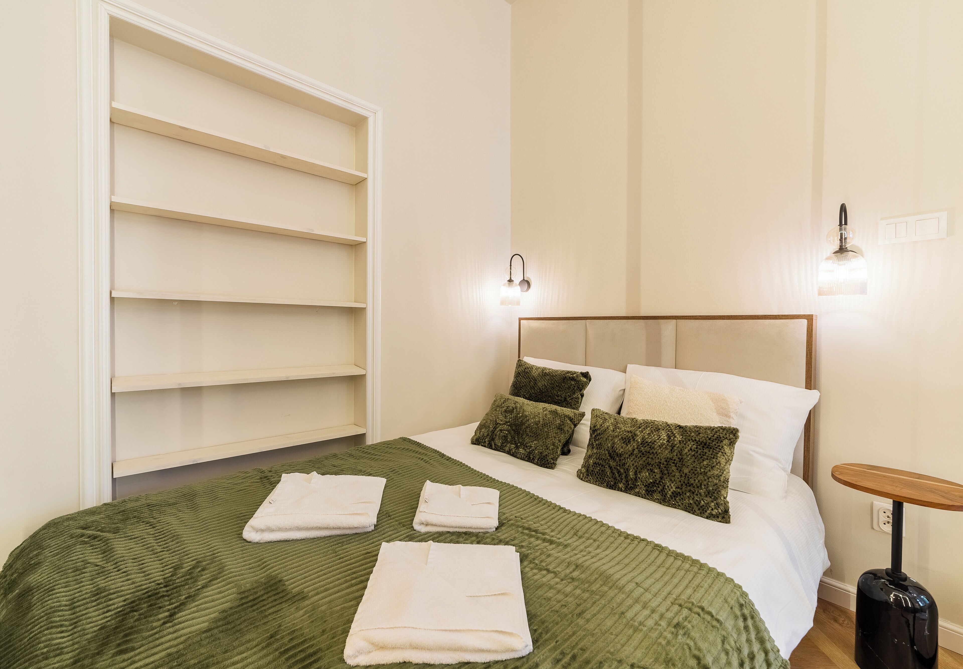 A hotel room with a bed, a wardrobe, and a bedside table.