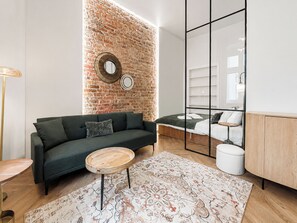 A modern living room with a brick wall, a sofa, a coffee table, and a bed with a headboard. - Różana City Center Studio (Poznań)
