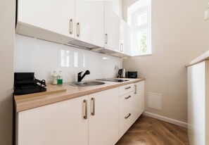 A modern kitchen with white cabinets, a stainless steel sink, a kettle, and a coffee maker. - Różana City Center Studio (Poznań)