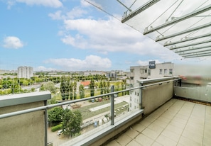 Un balcón con vistas a un paisaje urbano, que incluye edificios y zonas verdes.