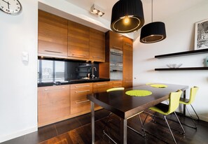 Een moderne keuken met houten kastjes, een zwart aanrecht en een eettafel met gele stoelen.