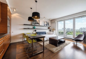 Een moderne woonkamer met een eethoek, een bank, een salontafel en een groot raam met uitzicht op de stad.
