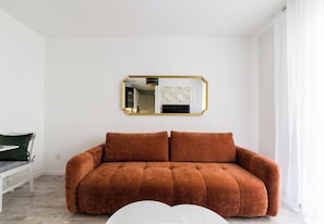 Ein Zimmer mit einem braunen Sofa, einer weißen Bank und einem Spiegel mit goldener Rahmung.