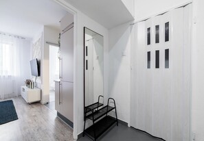 A modern, minimalist room with a large mirror, a black metal chair, and a white wardrobe with multiple doors. - Sikorskiego Signature Apartment (Poznań)