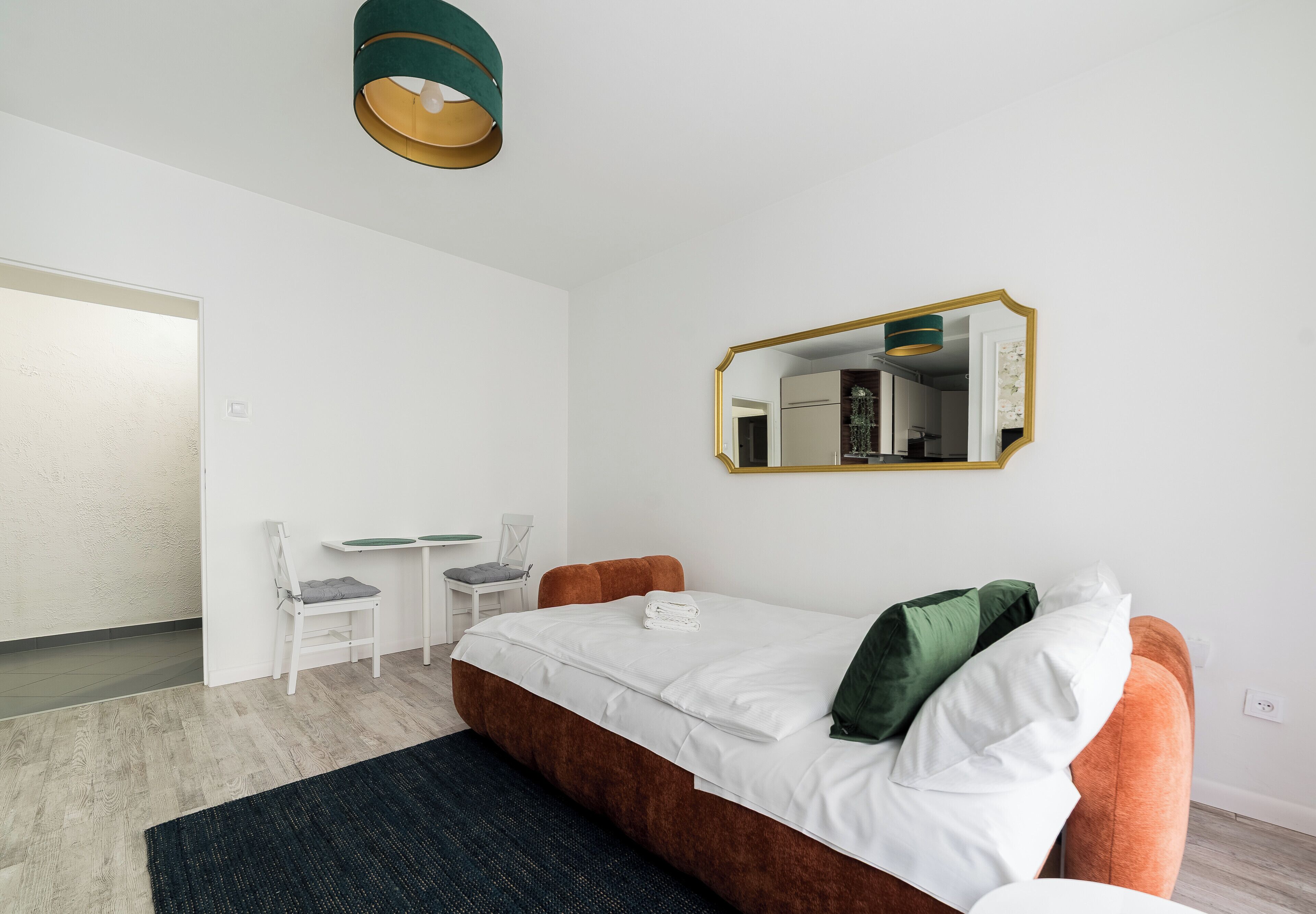 A hotel room with a bed, a desk, two chairs, a mirror, and a carpet.