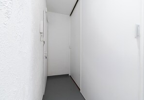 Ein schmaler Korridor mit weißen Wänden und dunklem Boden, der zu einer Tür am Ende führt.